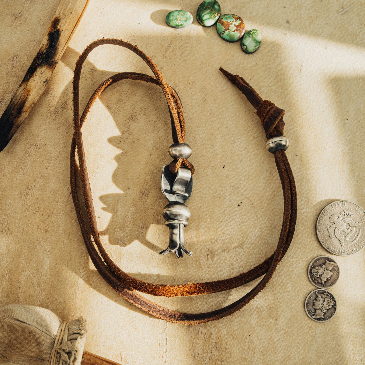 A hand-wrought sterling silver squash blossom pendant centered on an oval Sonoran Gold turquoise stone, its green face threaded with golden-brown matrix and set in a smooth bezel