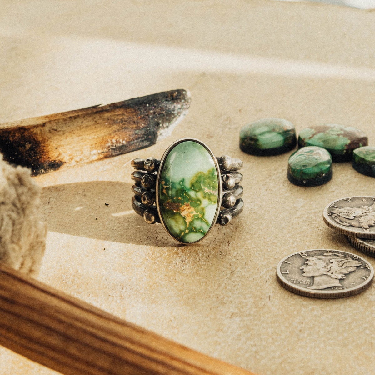 A hand-wrought sterling silver ring set with an oval Sonoran Gold turquoise stone, its green face threaded with golden-brown and rust matrix, set in a smooth straight bezel