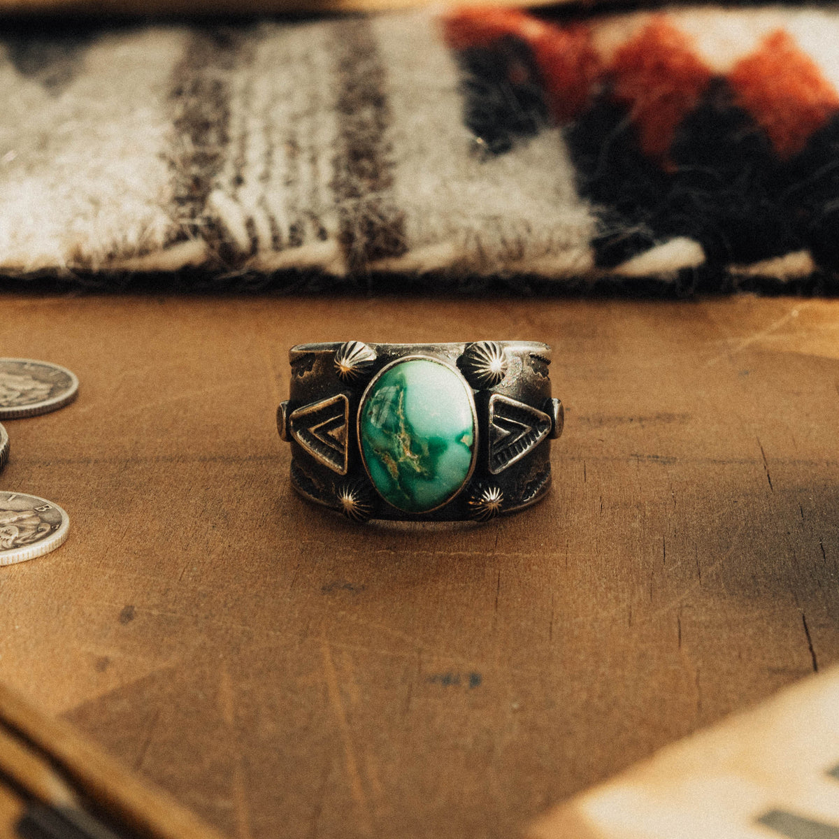 A hand-wrought sterling silver ring set with an oval Emerald Valley turquoise stone, its rich teal-green face threaded with golden-brown matrix, set in a smooth straight bezel