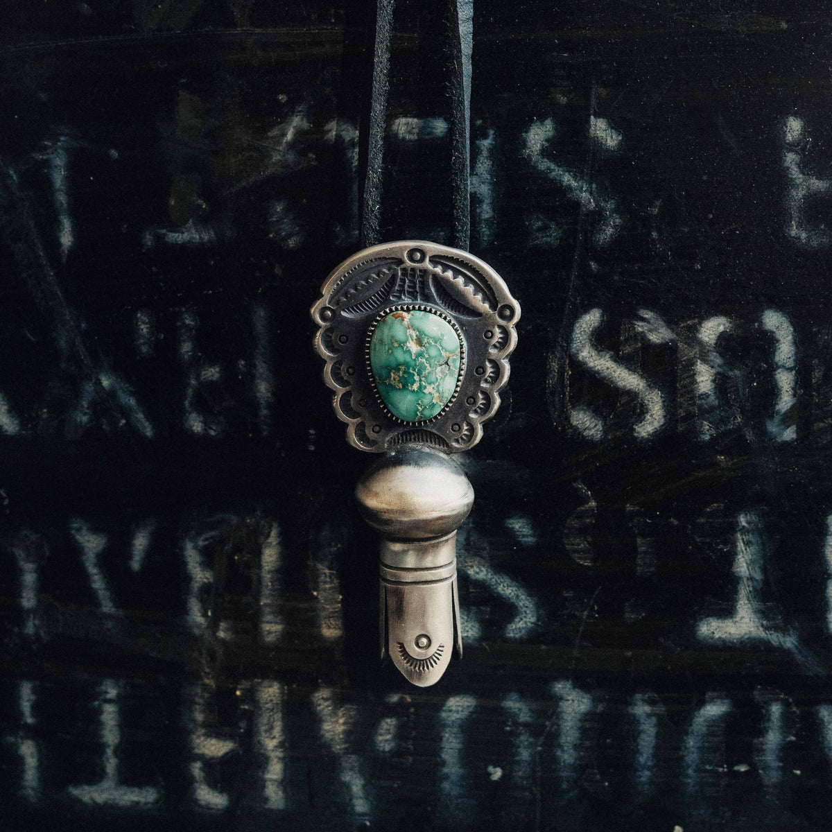 A hand-wrought sterling silver squash blossom pendant centered on a natural Fox turquoise stone, its green face veined with soft matrix and set in a hand-cut serrated bezel