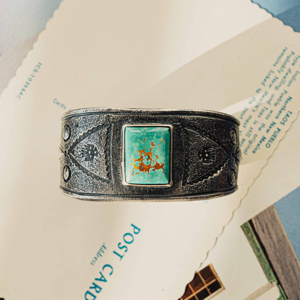 A wide tufa cast sterling silver cuff centered on a rectangular Royston turquoise stone, its soft green face threaded with rust-brown matrix, set in a smooth bezel