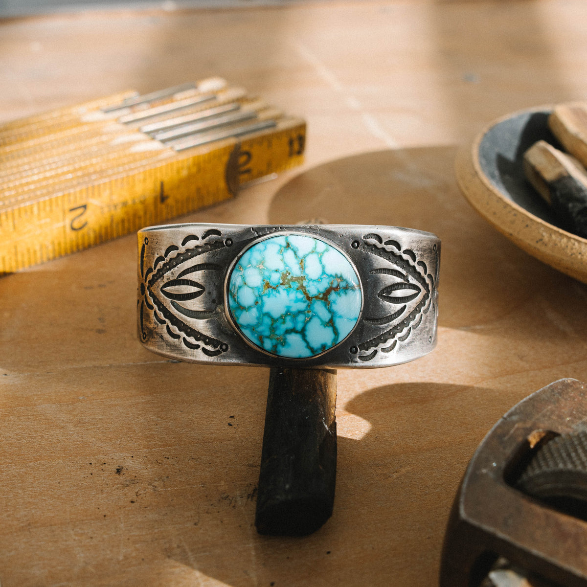 A tufa cast ingot cuff stamped with a set of our one-of-a-kind steel stamps set with a high grade Kingman Water Web turquoise stone One of a kind, now held in a private collection