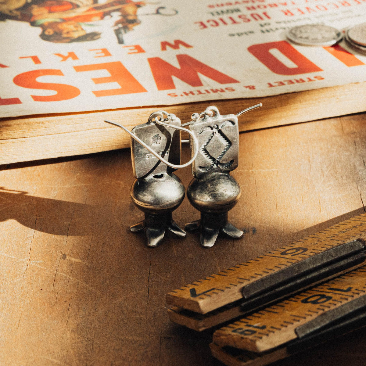 A pair of hand-wrought sterling silver squash blossom earrings, each featuring a stamped rectangular plate on the first tier, dressed with a diamond and rope stamp pattern and hung from a sterling French hook ear wire — view 3