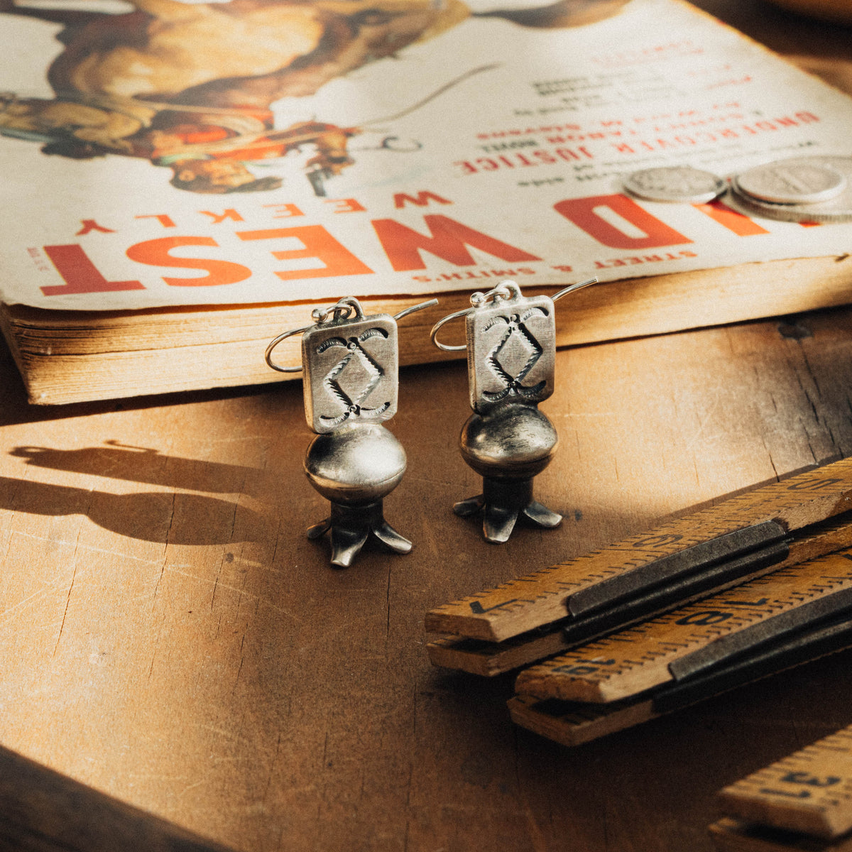 A pair of hand-wrought sterling silver squash blossom earrings, each featuring a stamped rectangular plate on the first tier, dressed with a diamond and rope stamp pattern and hung from a sterling French hook ear wire