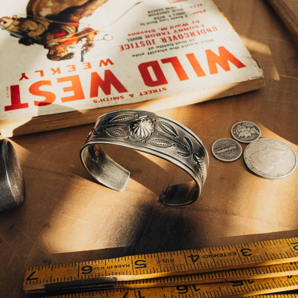 A hand-wrought sterling silver concho cuff, its wide face centered on a raised flower concho flanked on each side by a symmetrical arrangement of traditional stamp details and arrow accents, all worked in repoussé with bump-out details that lift the design from the surface — view 4