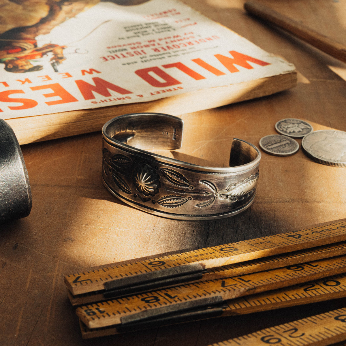 A hand-wrought sterling silver concho cuff, its wide face centered on a raised flower concho flanked on each side by a symmetrical arrangement of traditional stamp details and arrow accents, all worked in repoussé with bump-out details that lift the design from the surface — view 2