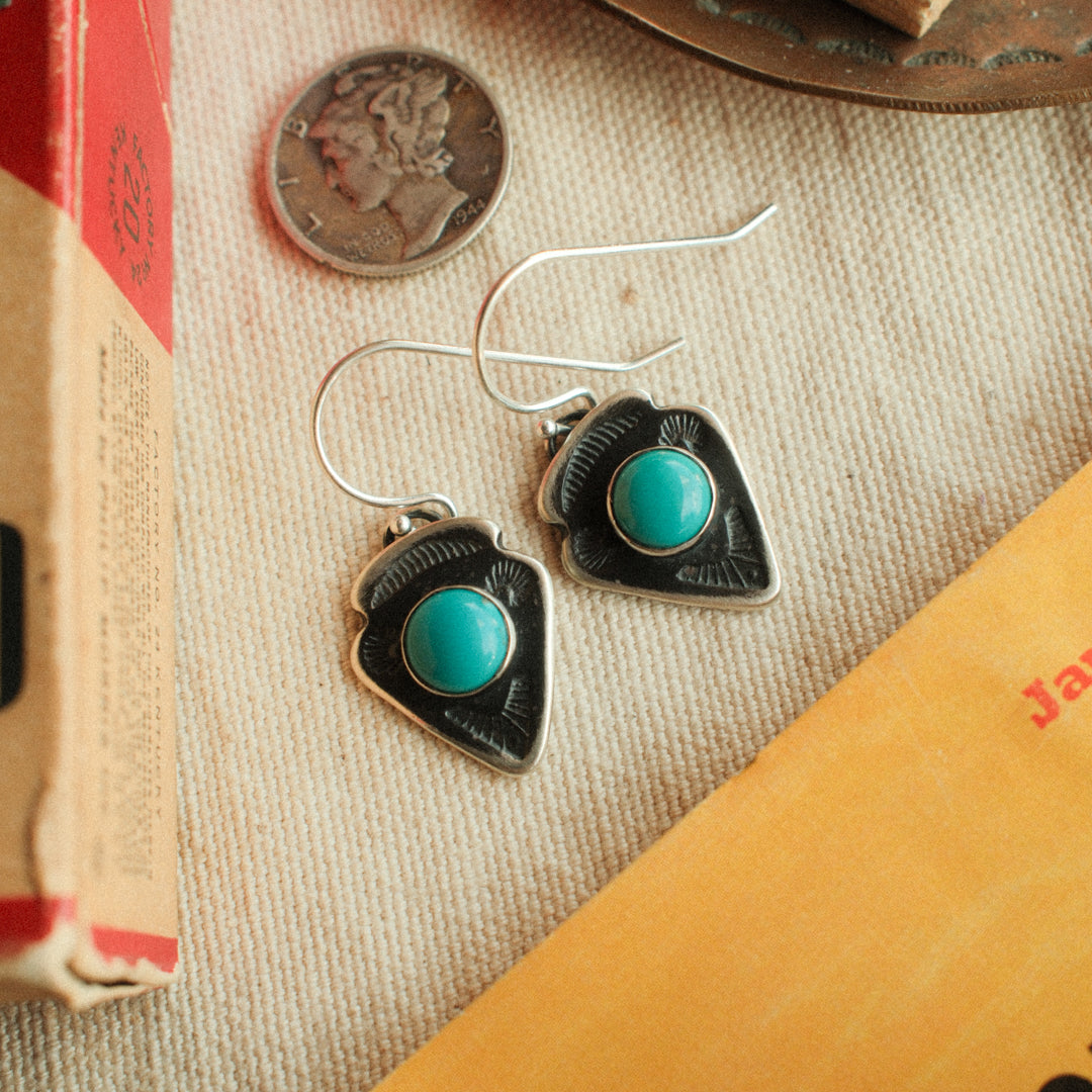 A pair of sterling silver arrowhead earrings with traditional stampwork and Lone Mountain turquoise centers, hung from French wires with a well-worn patina.