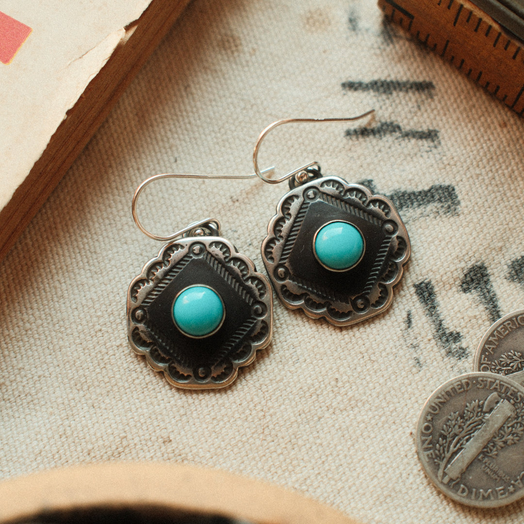 Vintage-inspired sterling silver earrings with scalloped corners, set with Lone Mountain turquoise and finished with a strong patina.