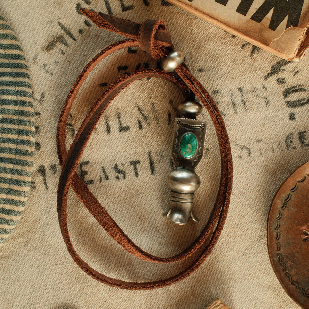 A one-of-a-kind hand-stamped squash blossom set with an 8×12mm premium piece of Fox turquoise, on brown leather with two handmade silver adjusting beads — view 2