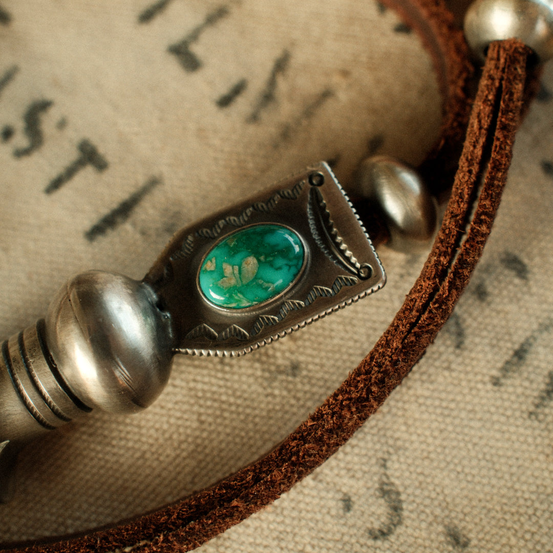 A one-of-a-kind hand-stamped squash blossom set with an 8×12mm premium piece of Fox turquoise, on brown leather with two handmade silver adjusting beads — view 5