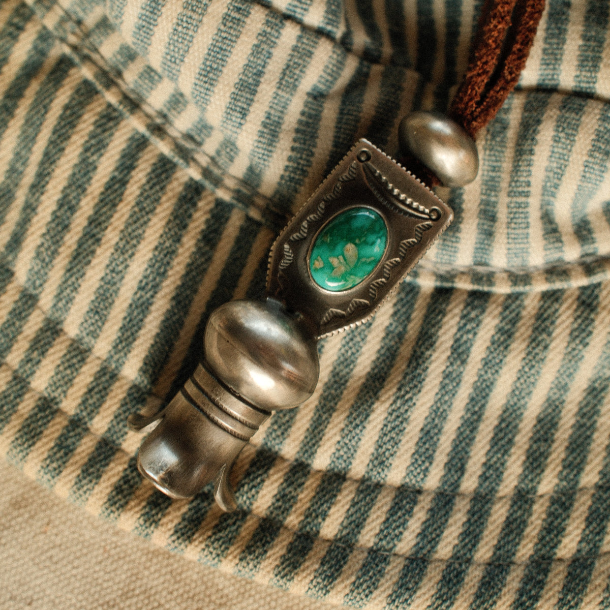 A one-of-a-kind hand-stamped squash blossom set with an 8×12mm premium piece of Fox turquoise, on brown leather with two handmade silver adjusting beads — view 3