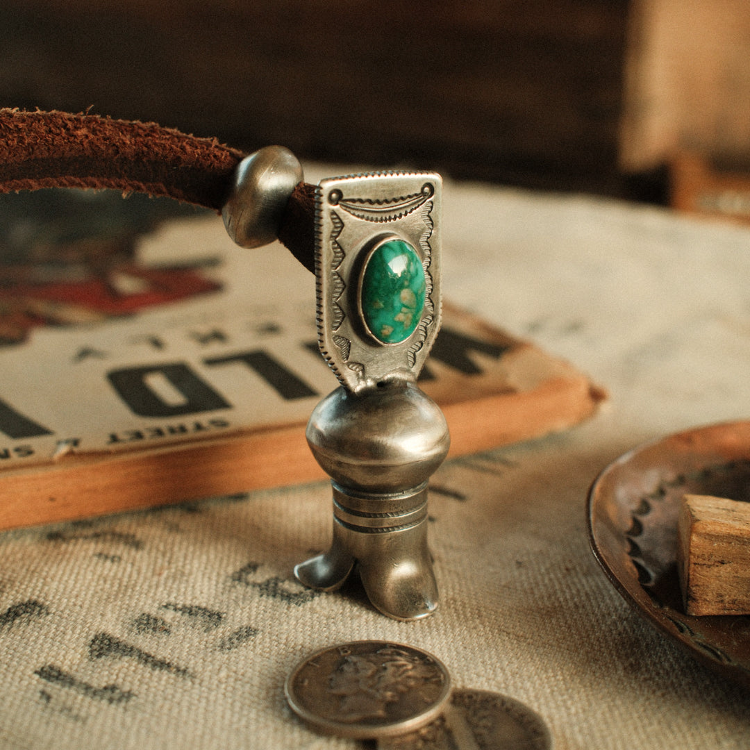 A one-of-a-kind hand-stamped squash blossom set with an 8×12mm premium piece of Fox turquoise, on brown leather with two handmade silver adjusting beads