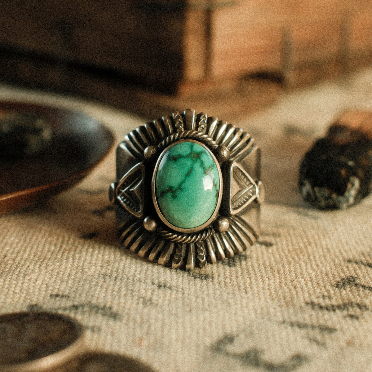 A Fox turquoise stone set in a smooth bezel inside a twisted rope border, framed by hand-stamped rays that fan out like a headdress