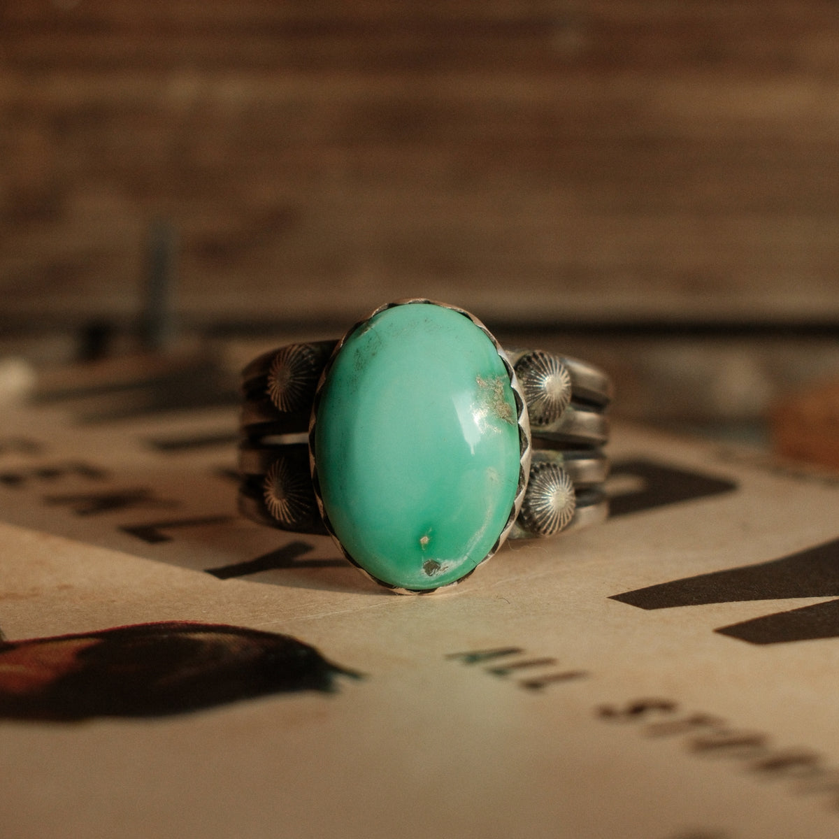 A one-of-a-kind 12×16mm Fox turquoise in a hand filed serrated bezel on a four-prong split shank with starburst conchos, stamped across the back
