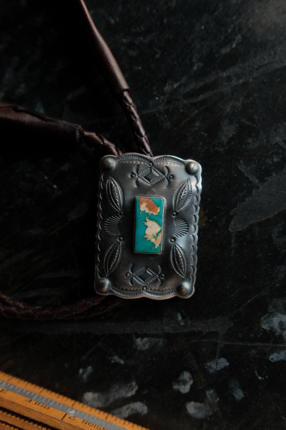 Royston turquoise from Nevada, hand-stamped with bump-outs for dimension and finished with leaf and concho detailing, set on a flat braided leather cord with silver tips